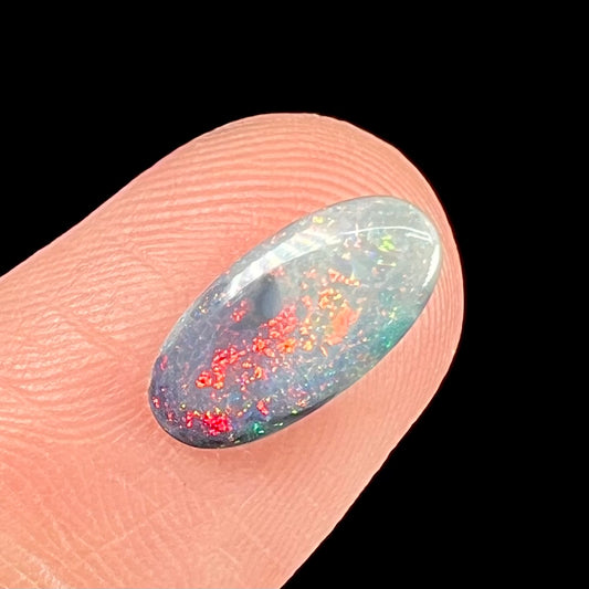 A loose, oval cabochon cut opal gemstone from Lightning Ridge, Australia.  The opal shines red and orange colors.