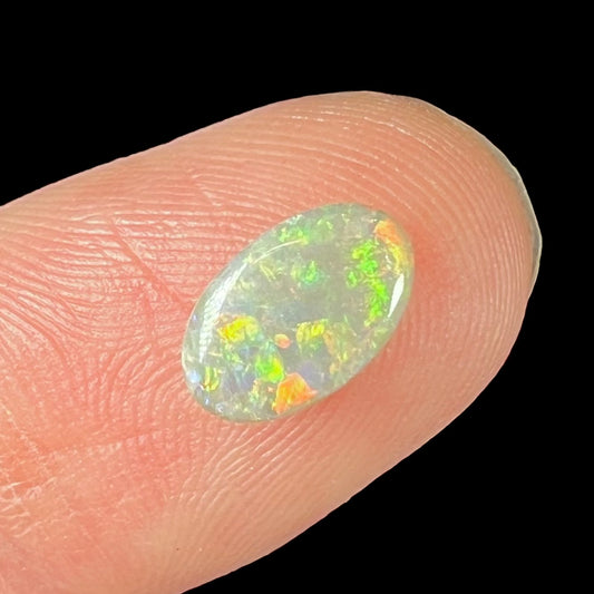 A loose, oval cabochon cut semi-black opal stone from Lightning Ridge, Australia.