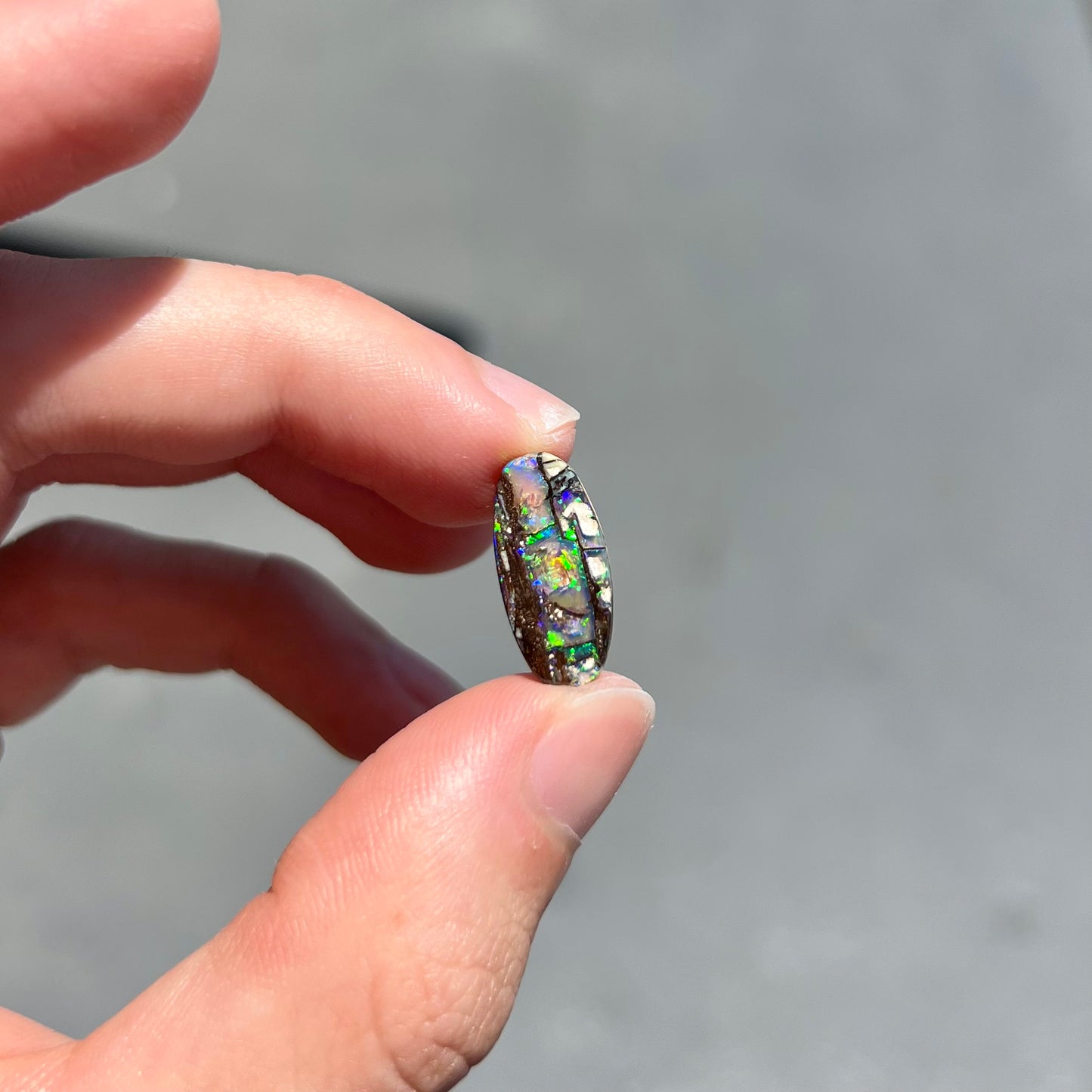 A loose, oval cut boulder opal stone from Koroit, Australia.  The opal shines green and blue colors.