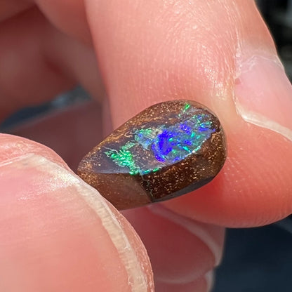 A loose, pear shaped boulder opal stone that flashes colors of green and blue.