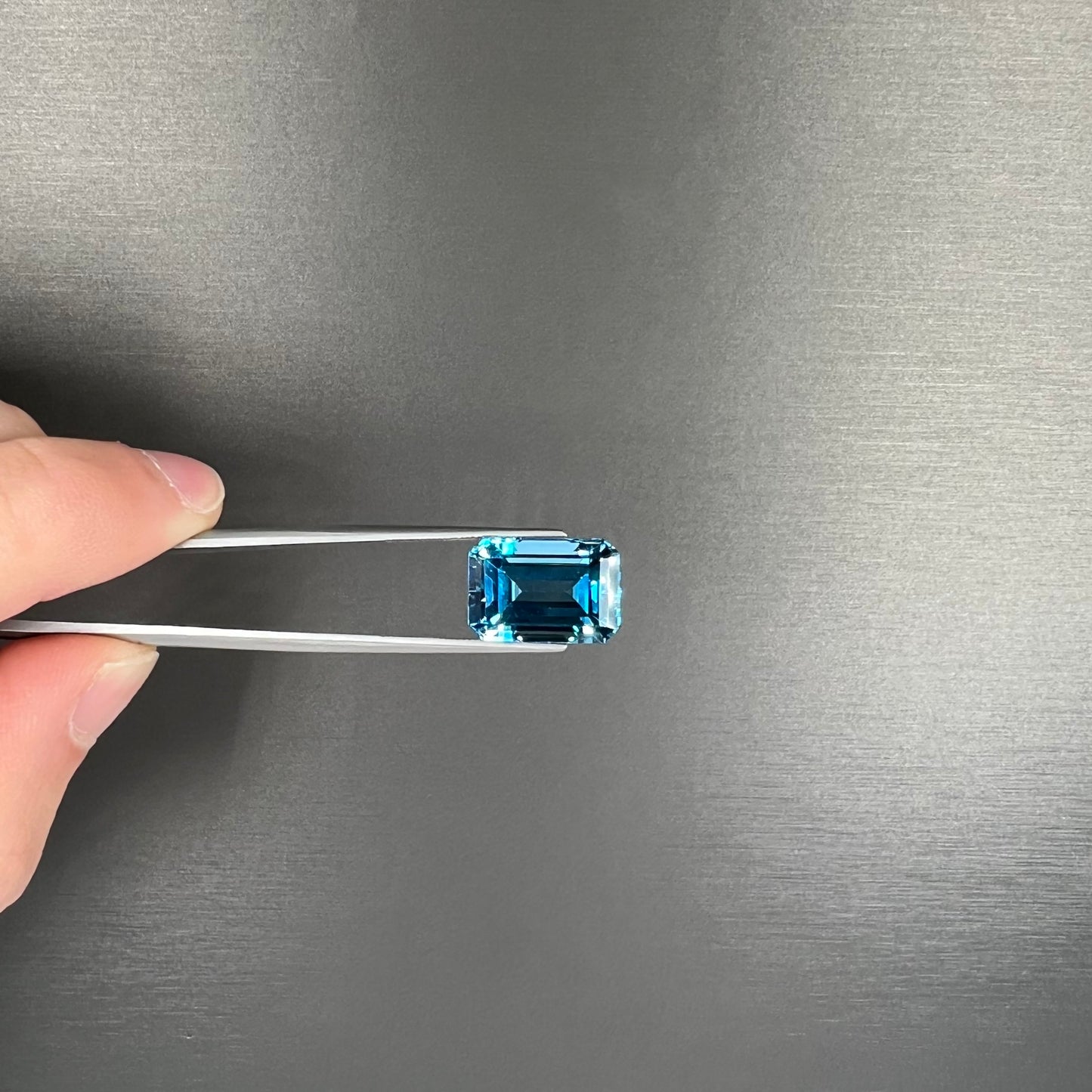 A loose, emerald cut London blue topaz gemstone.  The stone is a deep, dark blue color.