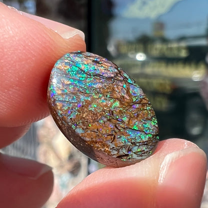 A loose, oval cabochon cut matrix boulder opal stone from Koroit, Australia.  The opal shines with green and blue colors.