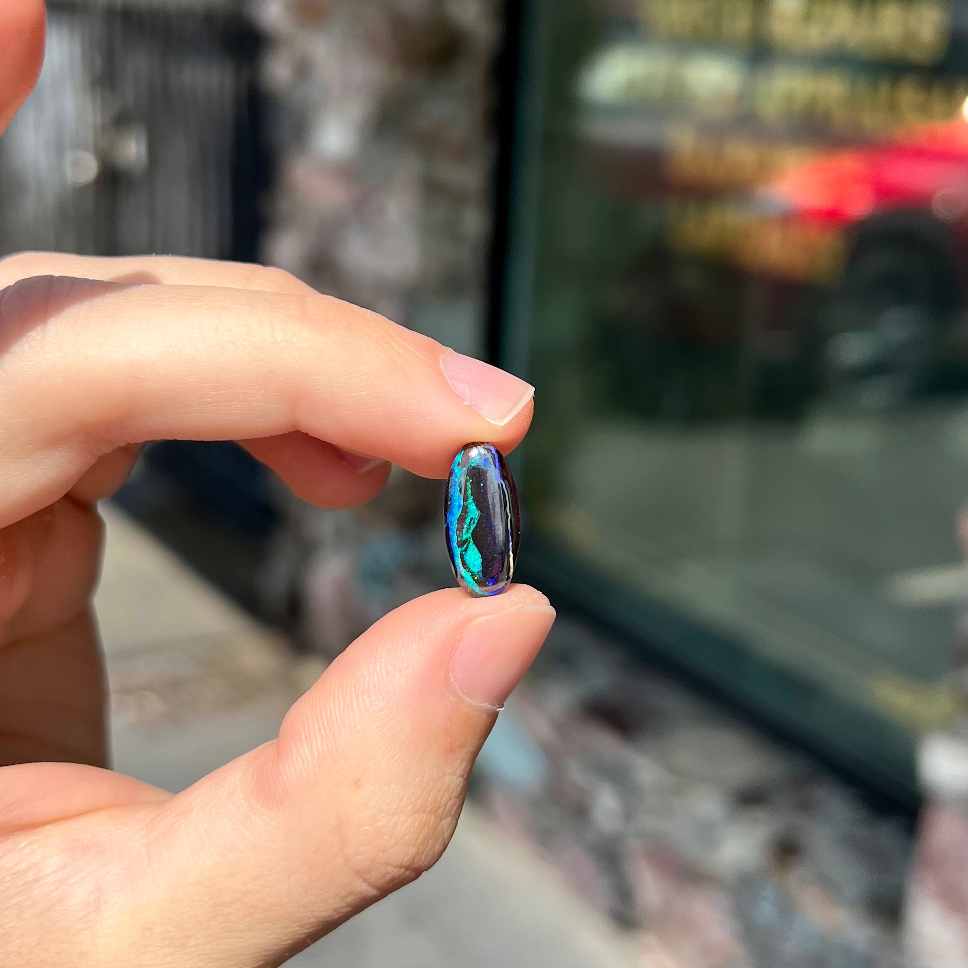 A loose, oval cabochon cut boulder opal stone.  The stone has bright blue and purple veins.