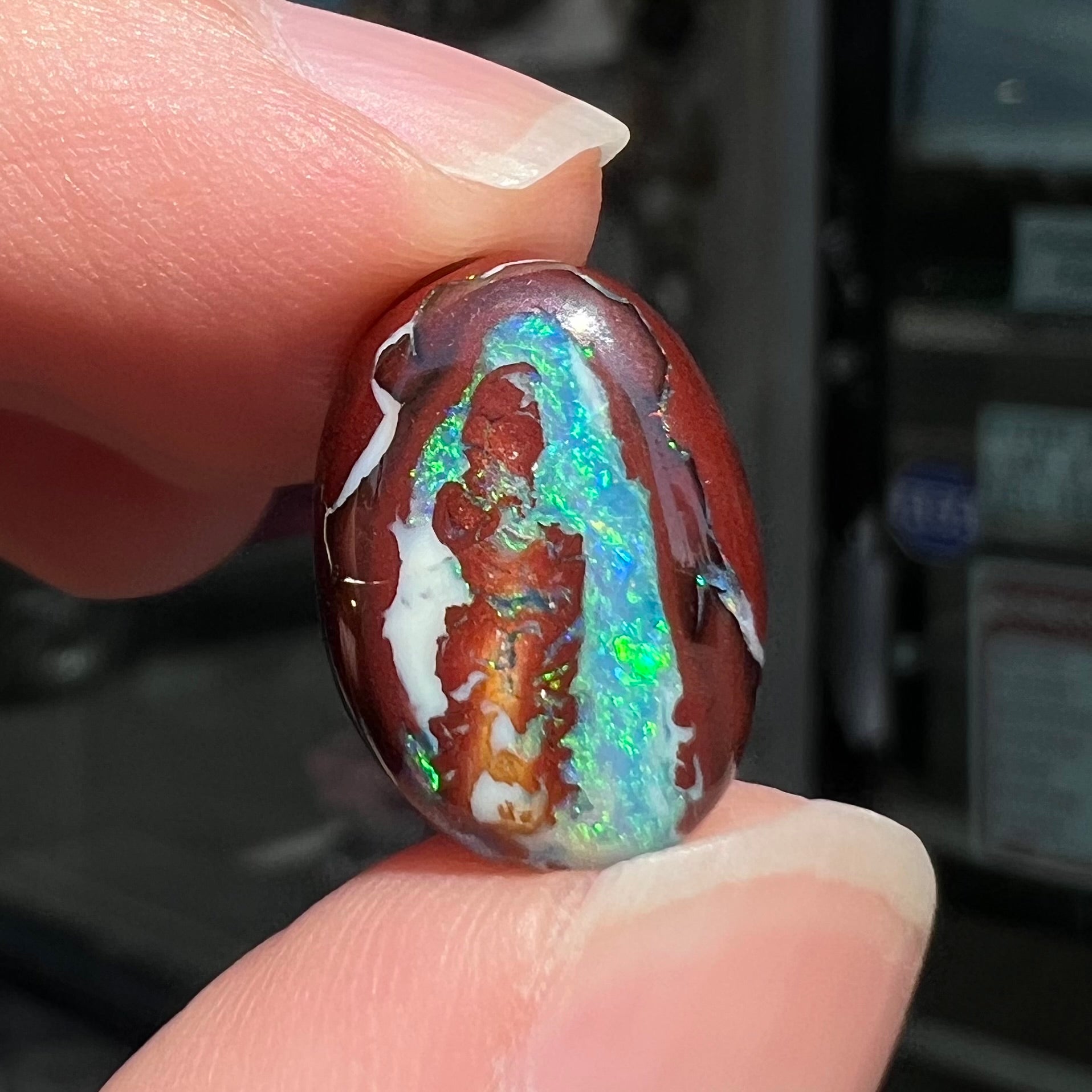 A loose, oval cabochon cut boulder opal stone from Australia.  The opal has blue and green veins in an ironstone matrix.