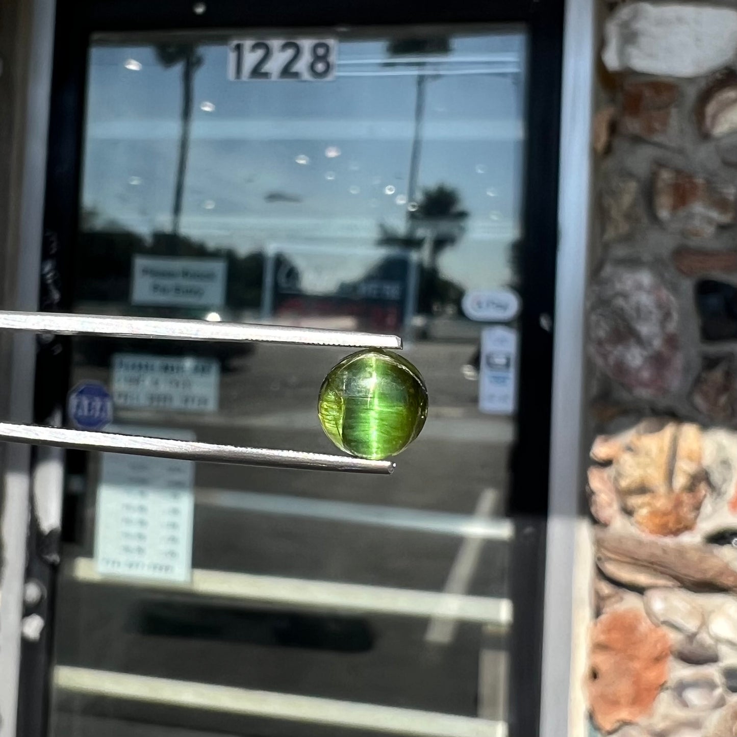 A loose, round cabochon cut green tourmaline stone that displays a cat's eye phenomenon.