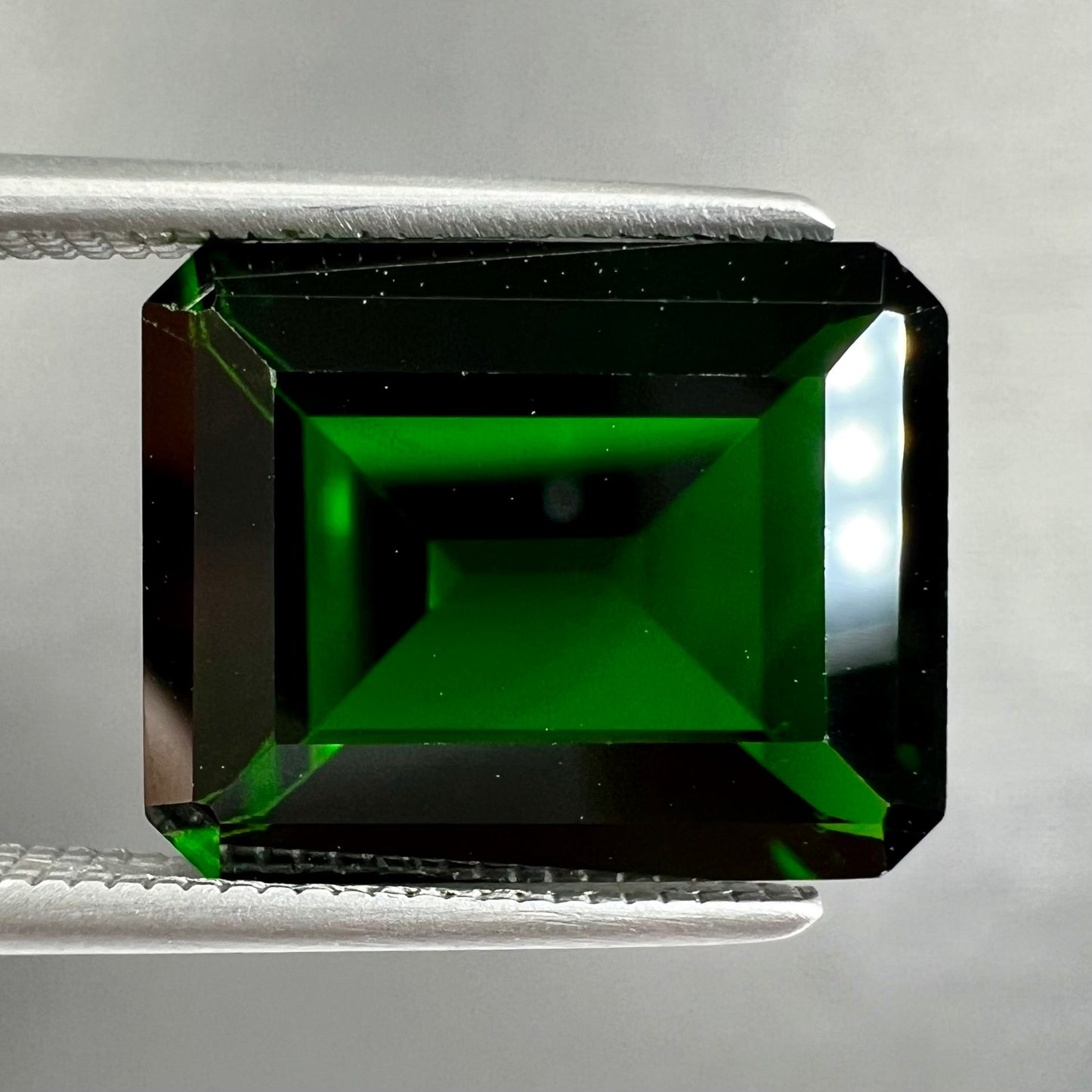 A large, emerald cut chrome diopside gemstone.  The gem is dark green color.