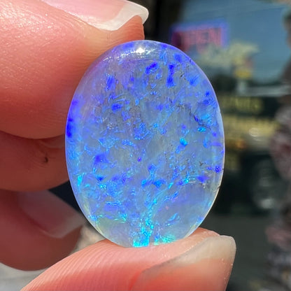 A loose, oval cabochon cut crystal opal from Lightning Ridge, Austalia that weighs 5.16 carats.  The stone has blue and purple colors.