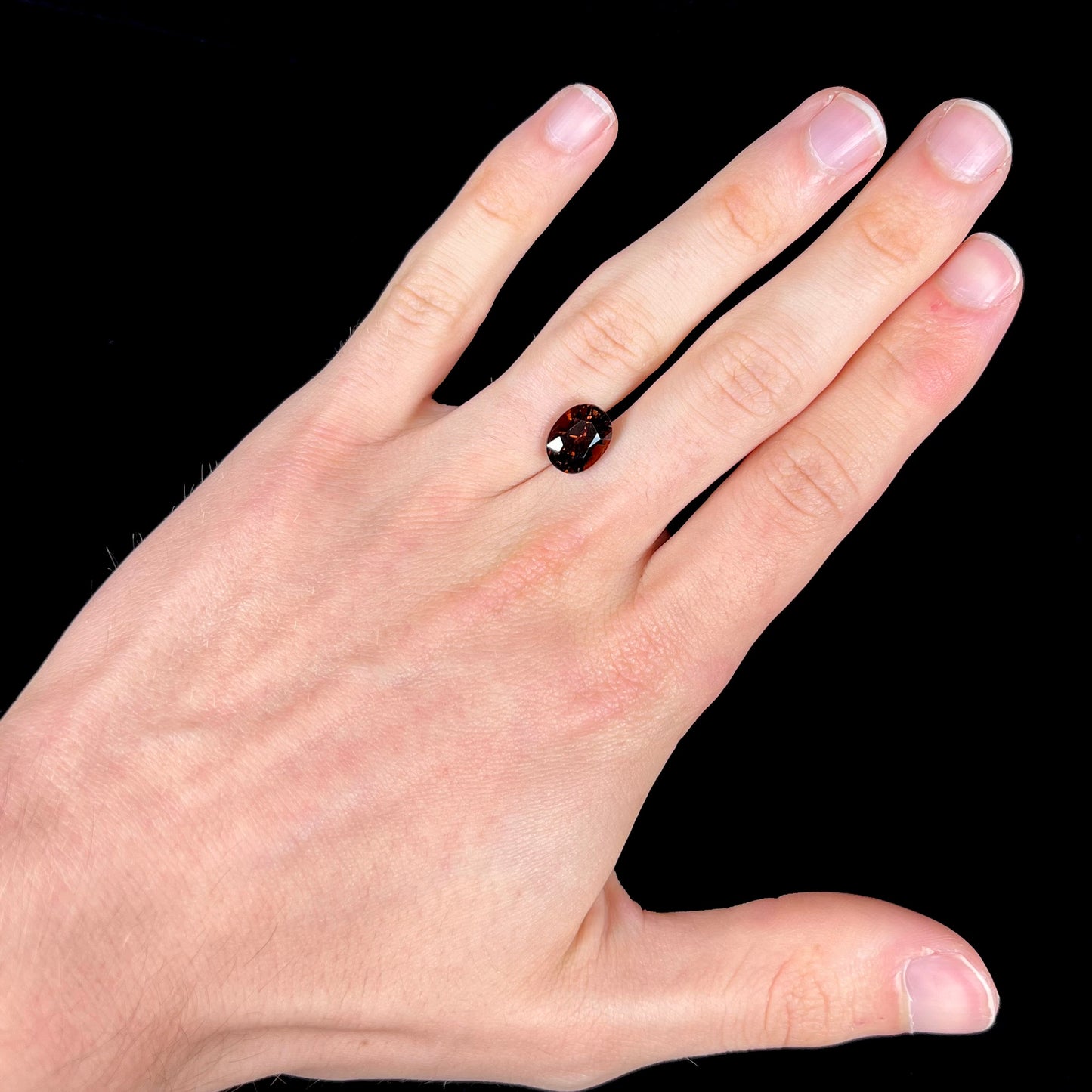 A loose, faceted oval cut dravite tourmaline gemstone.  The stone is a dark brown color with a purple secondary color.