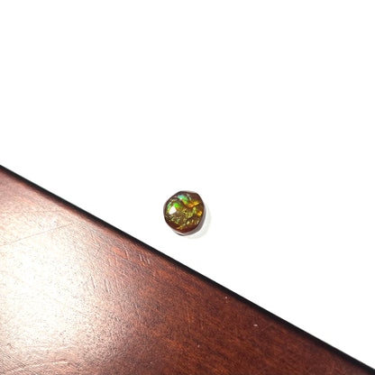 An iridescent green, yellow, and red Mexican fire agate stone.  The stone is an off-round cabochon.