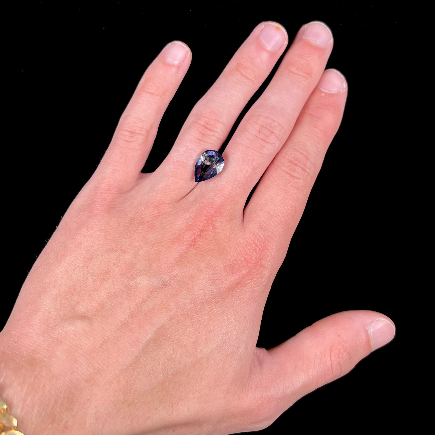 A loose, pear shaped bicolor iolite gemstone.  The stone shows violite purple and silver colors.