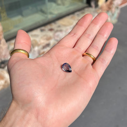 A loose, pear shaped bicolor iolite gemstone.  The stone shows violite purple and silver colors.