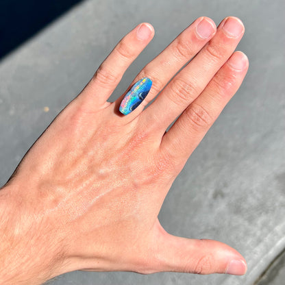 A barrel shaped boulder opal gemstone with a rainbow of colors.