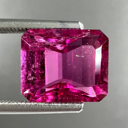 A loose, faceted modified emerald cut hot pink tourmaline stone.