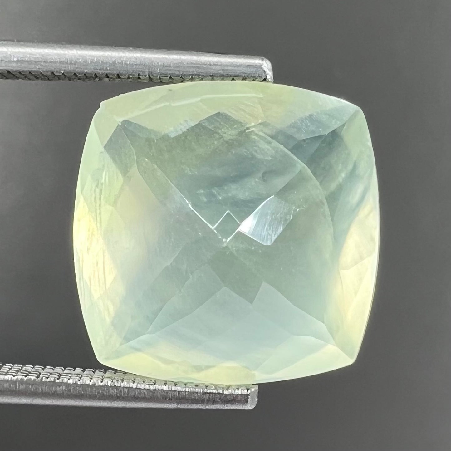 A loose, faceted checkerboard cushion cut green prehnite stone.  The stone is sleepy yellowish green.