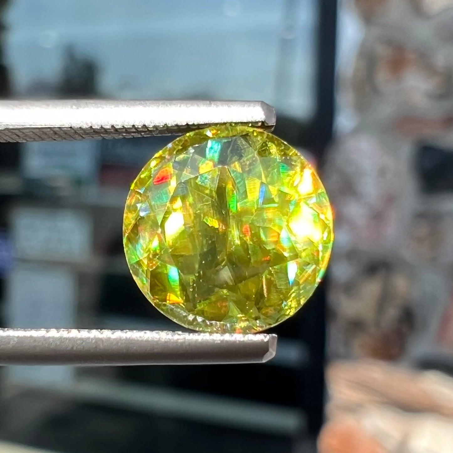 A loose, round brilliant cut sphene gemstone.  The stone is green with orange, green, blue, and yellow flashes.