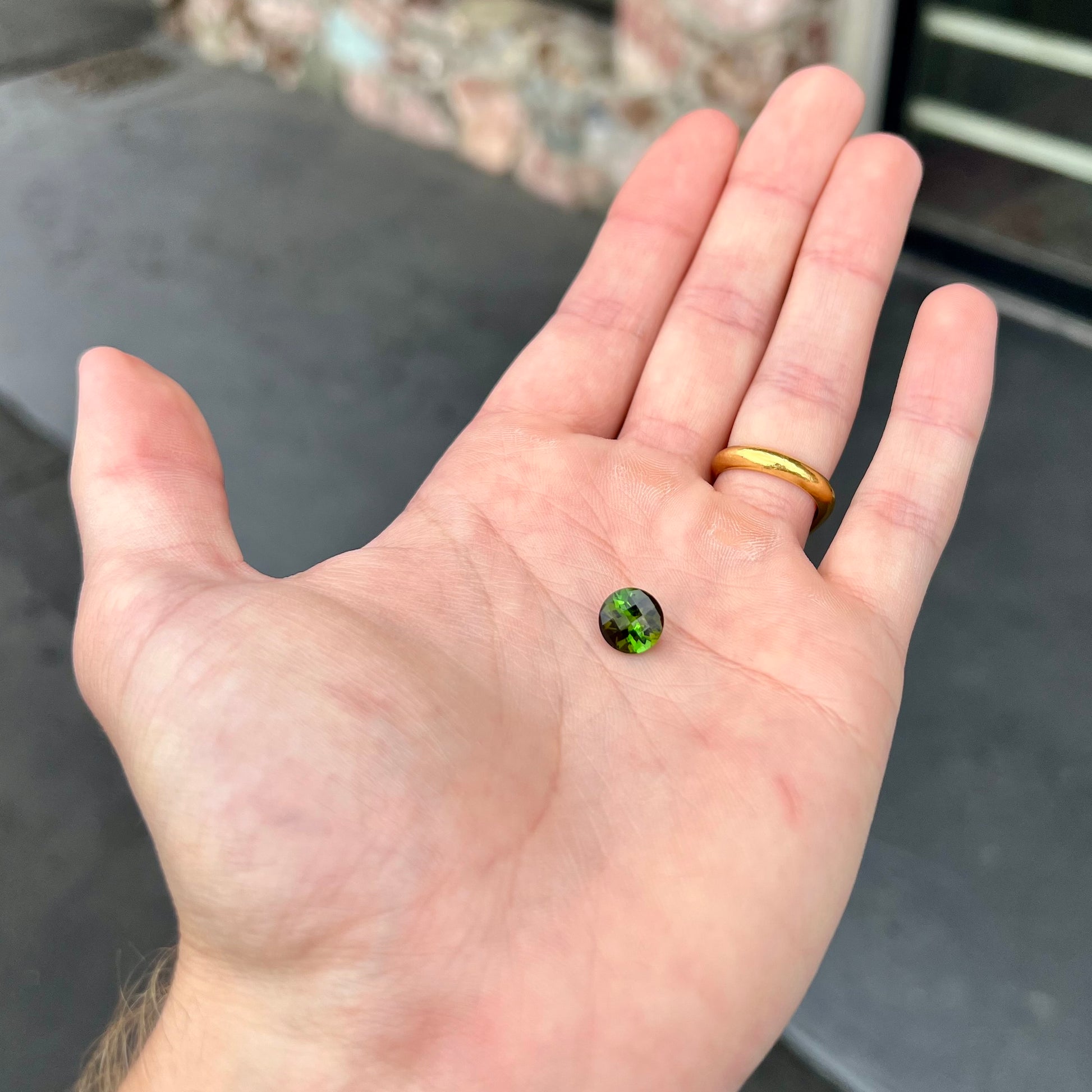 A loose, round checkerboard cut green tourmaline stone with flashes of yellow.