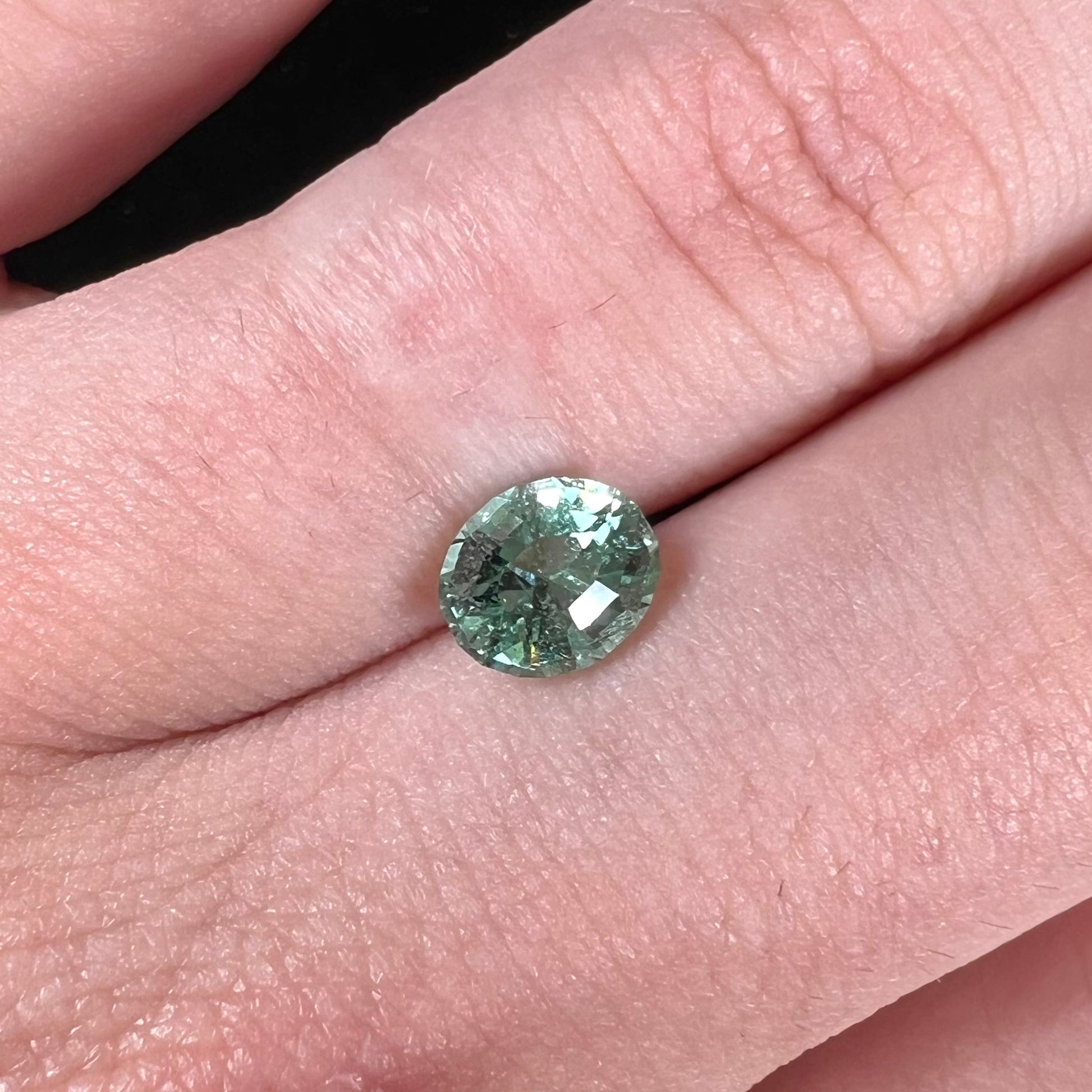 A loose, faceted modified oval cut mint green tourmaline gemstone.