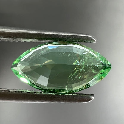 A faceted marquise cut electric green tourmaline gemstone.  The stone has an eye-visible rutile needle inclusion.