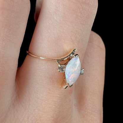 A yellow gold marquise cut opal ring set with two white sapphire accent stones.