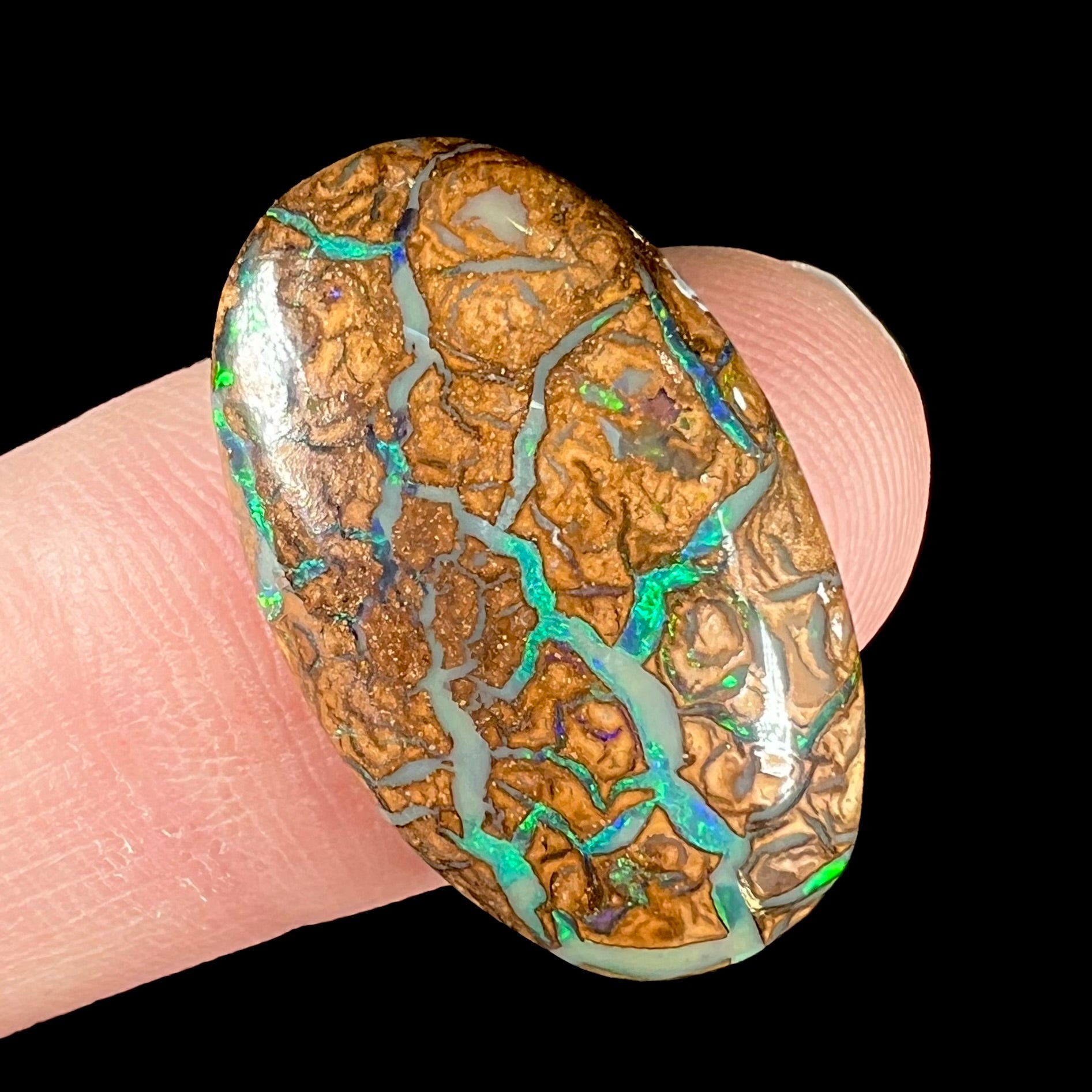 A loose, oval cabochon cut boulder opal from Koroit, Australia.  The opal has green flashes and blue veins.