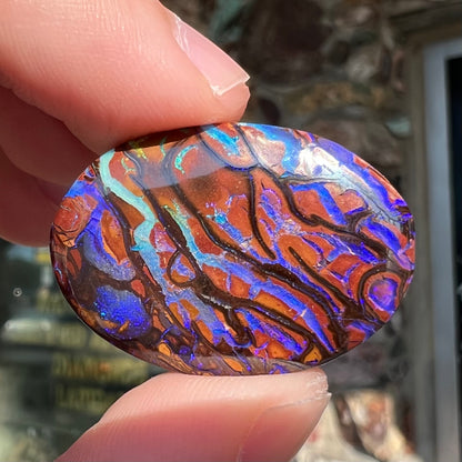 A loose, oval cabochon cut boulder opal from Koroit, Australia.  The opal has violet and purple veins.