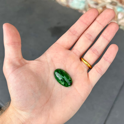 A loose, oval cabochon cut green maw sit sit stone.