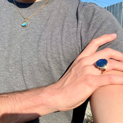 A large, unisex gold ring mounted with a half-bezel set black opal doublet and diamonds.