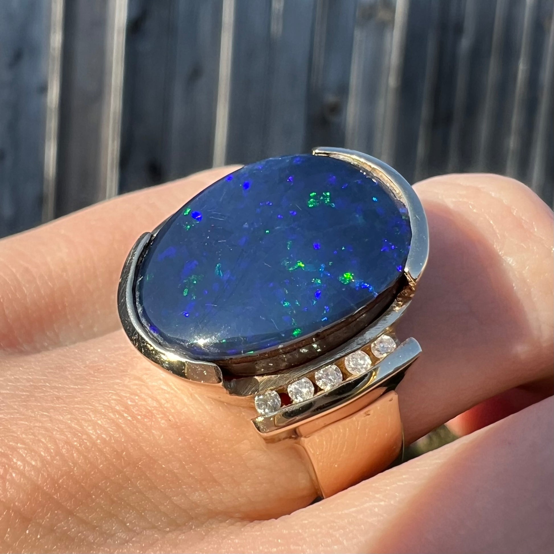 A large, unisex gold ring mounted with a half-bezel set black opal doublet and diamonds.