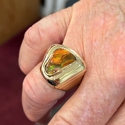 A heavy, yellow gold men's ring mounted with a Mexican fire agate stone.  The fire agate has orange, green, red, and purple colors.