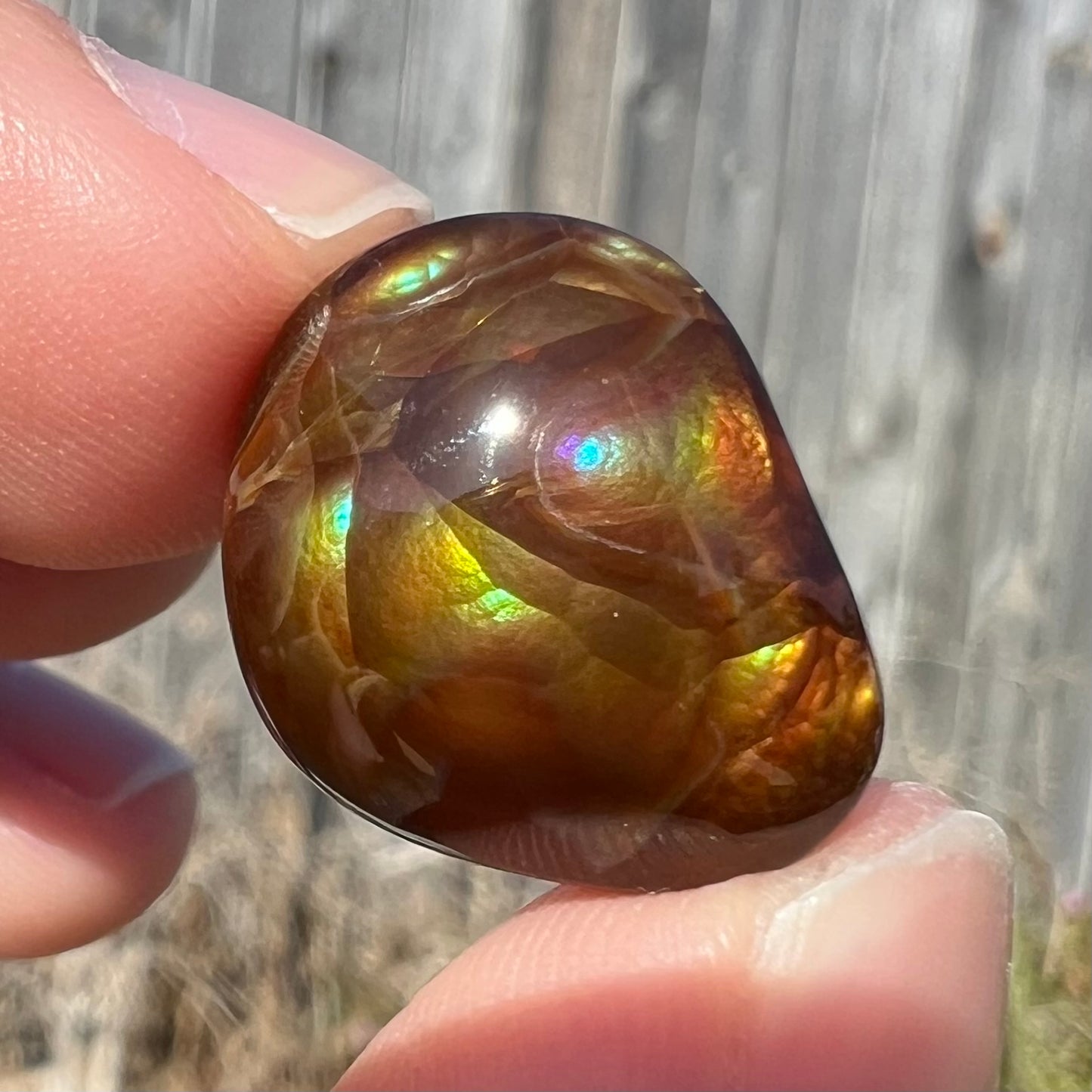 A large, round freeform shaped Mexican fire agate stone.  The stone has green, orange, purple, and blue iridescence.