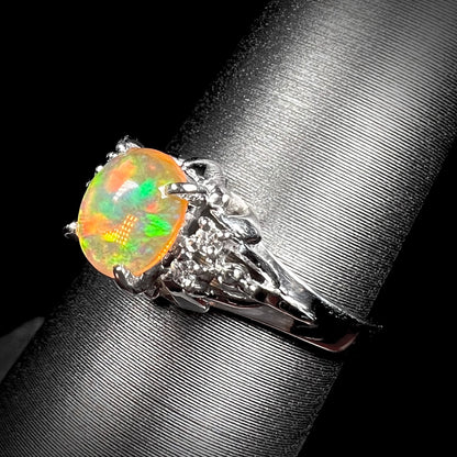 A platinum, diamond accented ring prong-set with an oval cabochon cut Mexican fire opal.