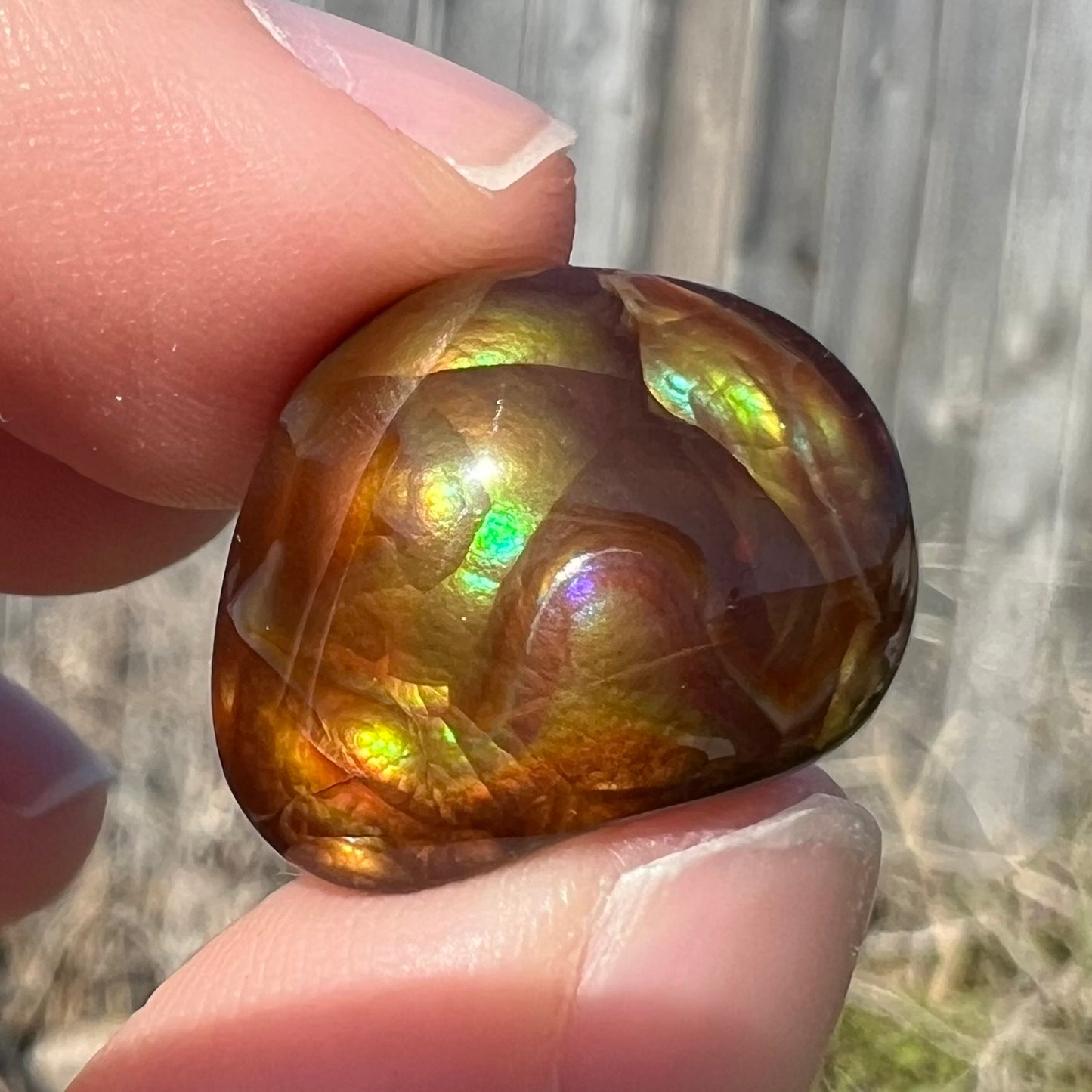 A large, round freeform shaped Mexican fire agate stone.  The stone has green, orange, purple, and blue iridescence.