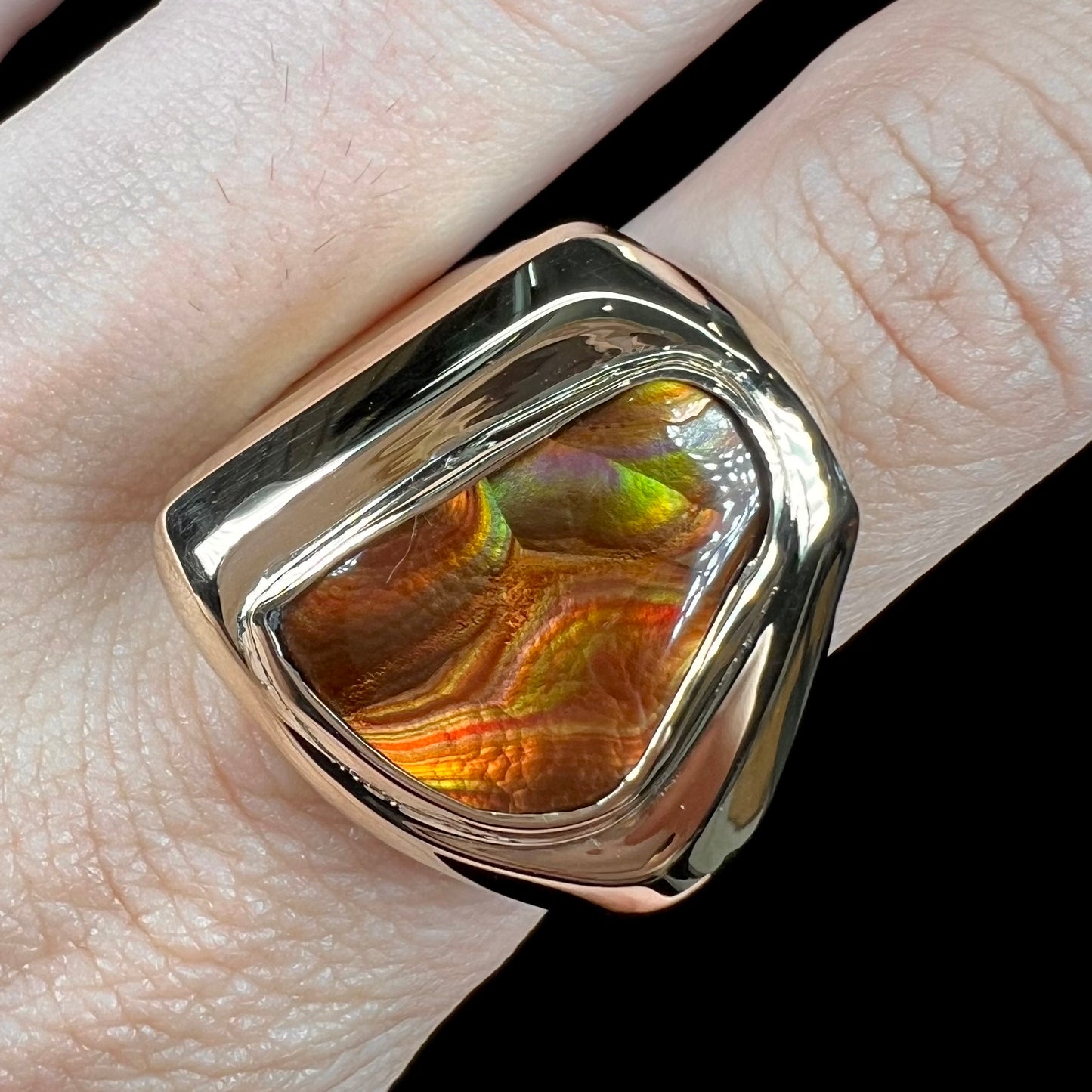 A heavy, yellow gold men's ring mounted with a Mexican fire agate stone.  The fire agate has orange, green, red, and purple colors.