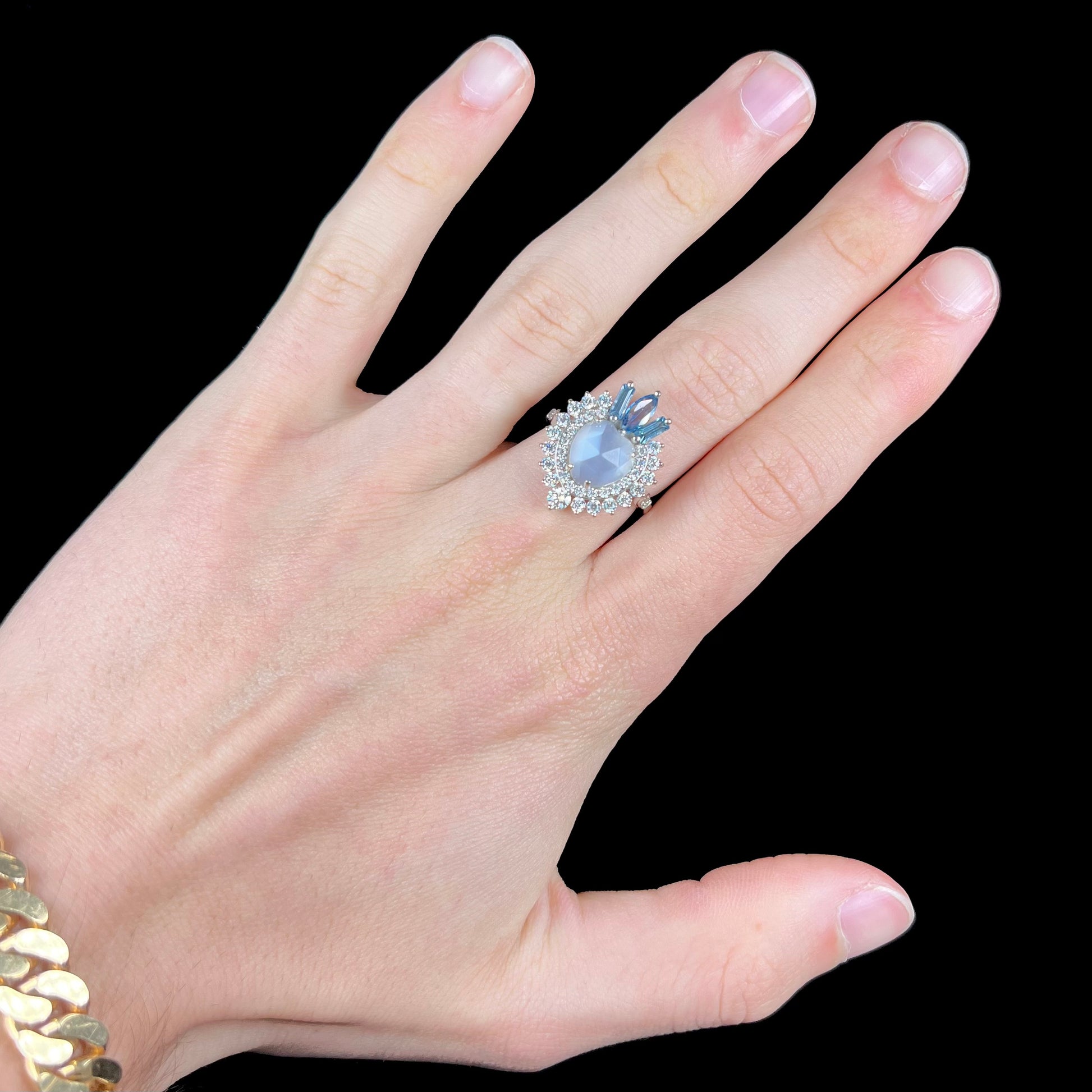 A ladies' white gold ring set with a faceted, heart shaped white moonstone, round moissanites, two aquamarine baguettes, and a marquise cut blue sapphire.