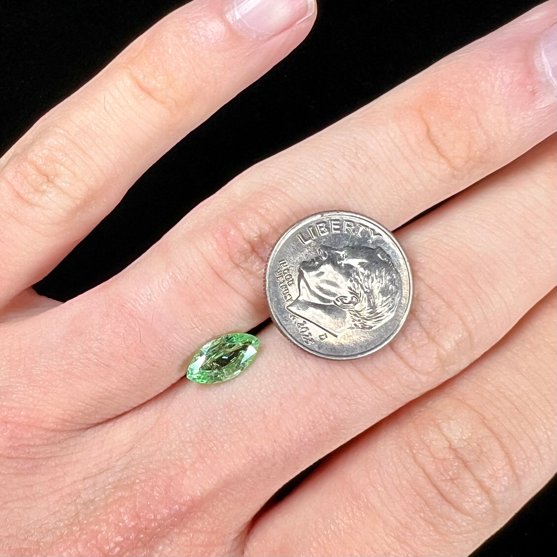 A faceted marquise cut electric green tourmaline gemstone.  The stone has an eye-visible rutile needle inclusion.