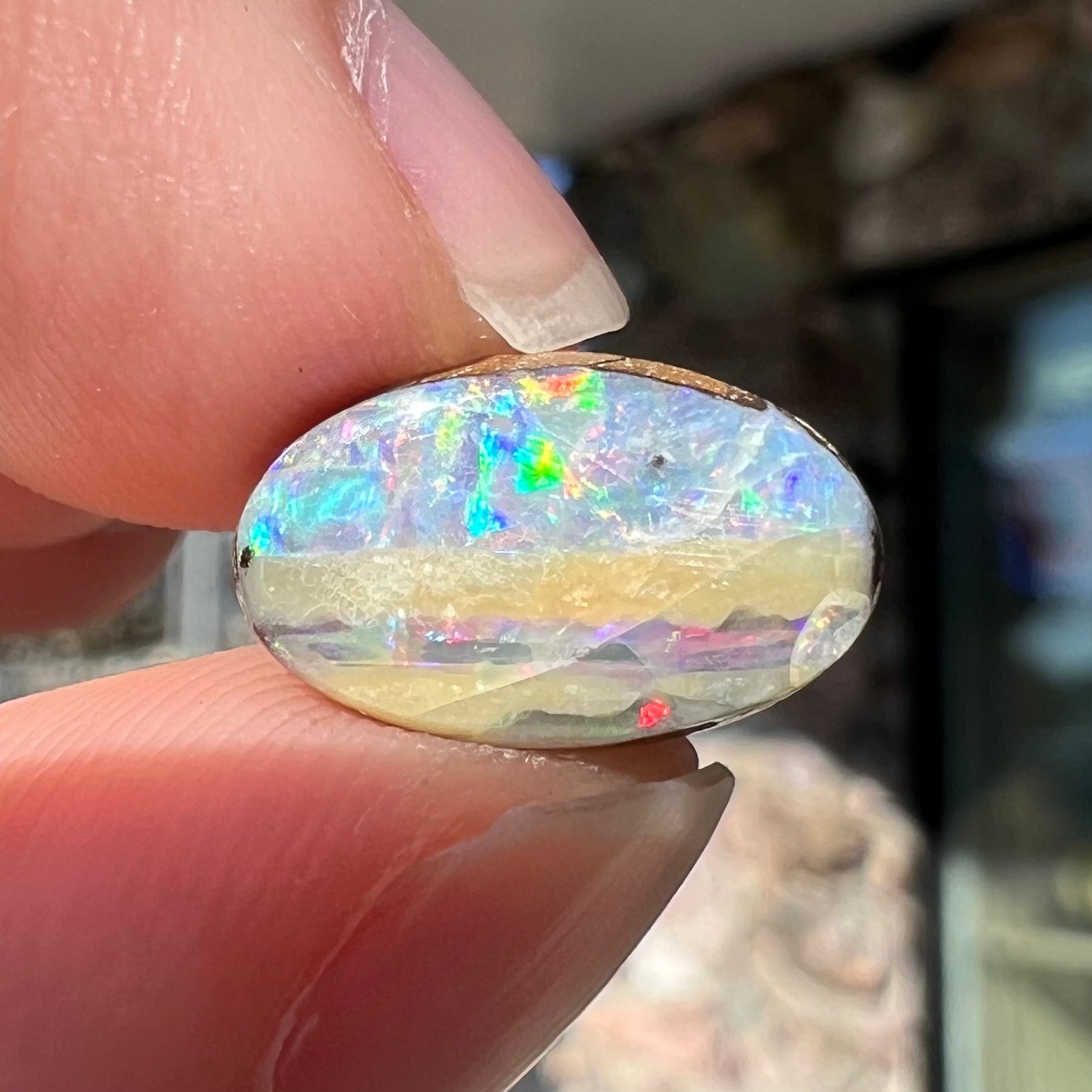 An oval cabochon cut boulder opal from Quilpie, Australia.  The opal has multicolor color play.