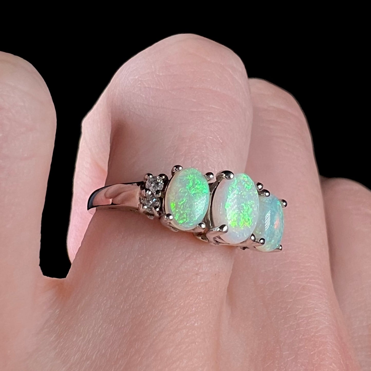 A ladies' white gold ring prong-set with three natural white opals and diamond accents.  The opals play a green color.