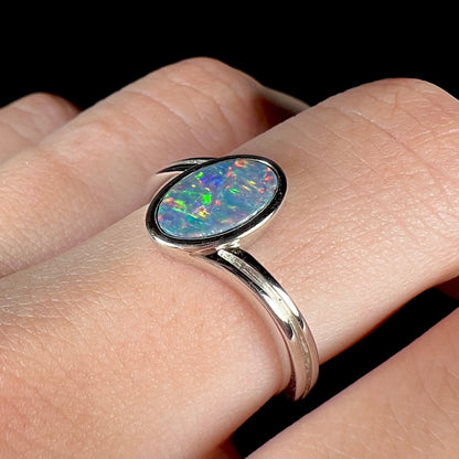 A sterling silver ring bezel-set with an oval shaped black opal doublet.  The opal has red and blue fire.