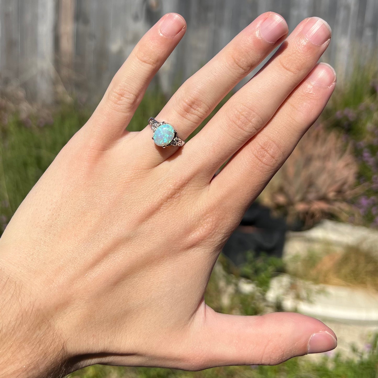 A platinum filigree ring mounted with a blue-green crystal opal and diamond accents.