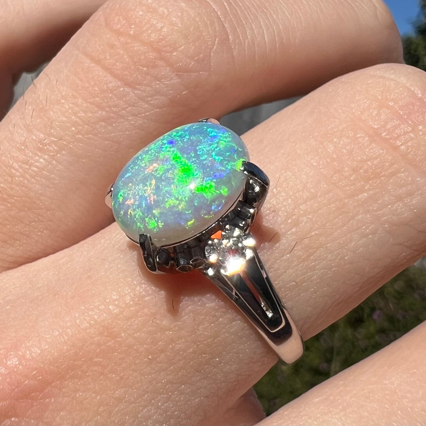 A platinum filigree opal engagement ring set with diamond accents.  The opal has green-blue colors.