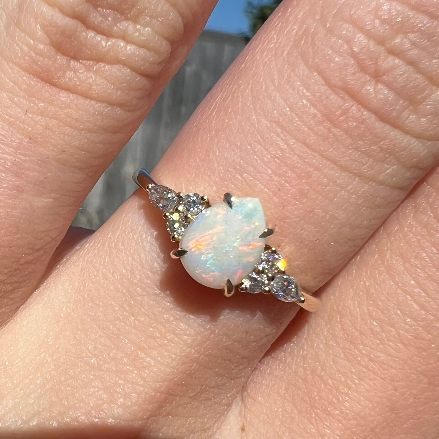 A dainty, pear shaped opal ring mounted in yellow gold with moissanite accents.