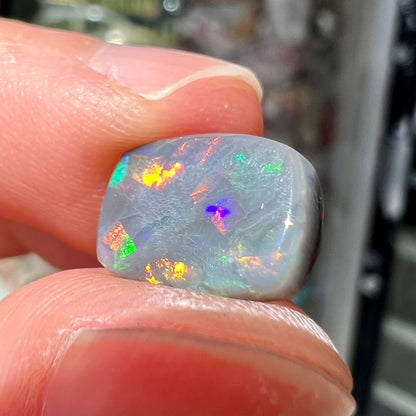 A loose, cushion cut black opal stone.  The stone plays colors of red, green, blue, and purple.