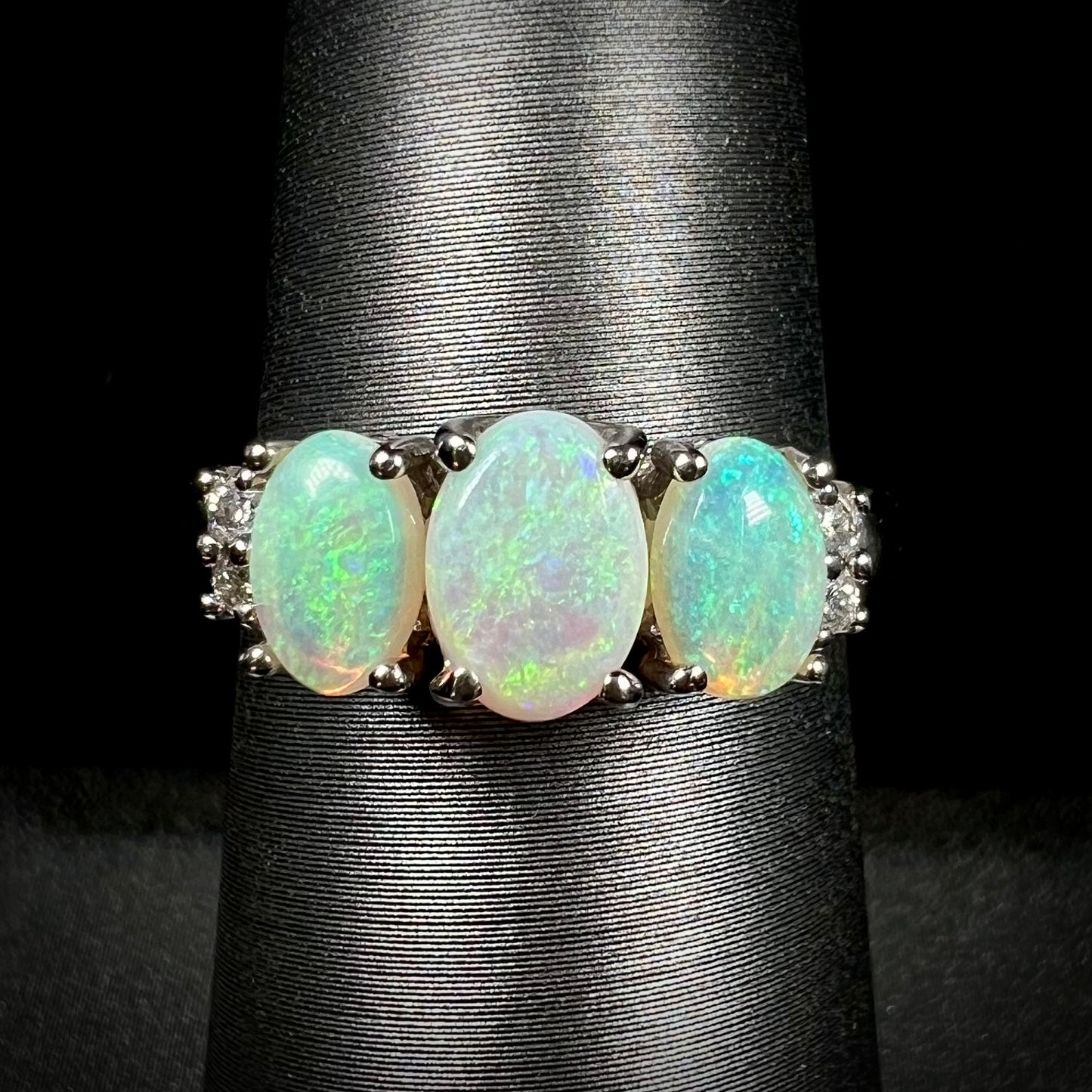 A ladies' white gold ring prong-set with three natural white opals and diamond accents.  The opals play a green color.