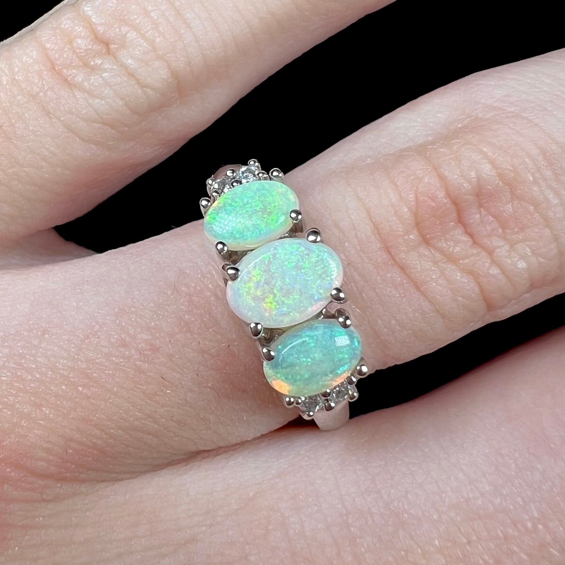 A ladies' white gold ring prong-set with three natural white opals and diamond accents.  The opals play a green color.