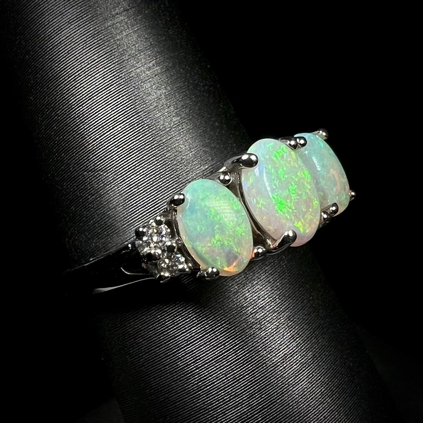 A ladies' white gold ring prong-set with three natural white opals and diamond accents.  The opals play a green color.