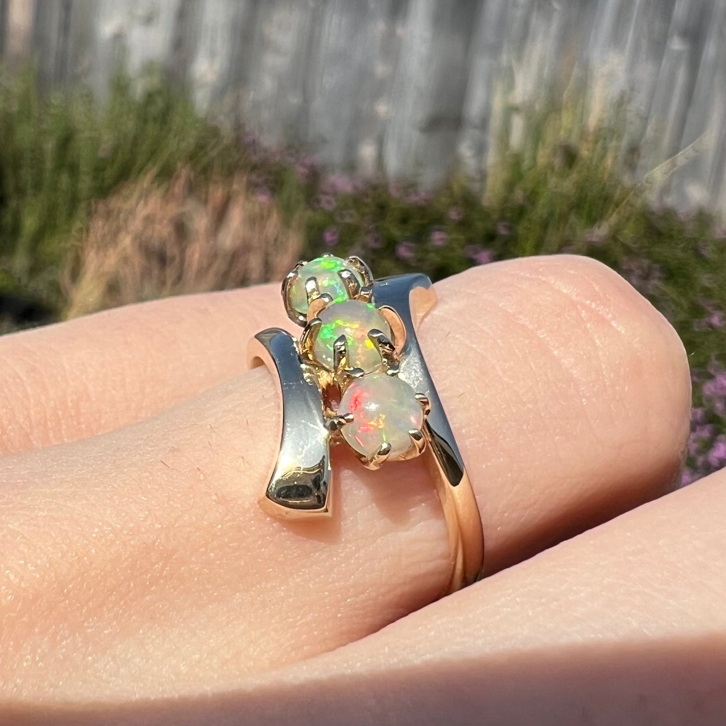 A yellow gold bypass shank ring mounted with three round cabochon cut Ethiopian fire opals.