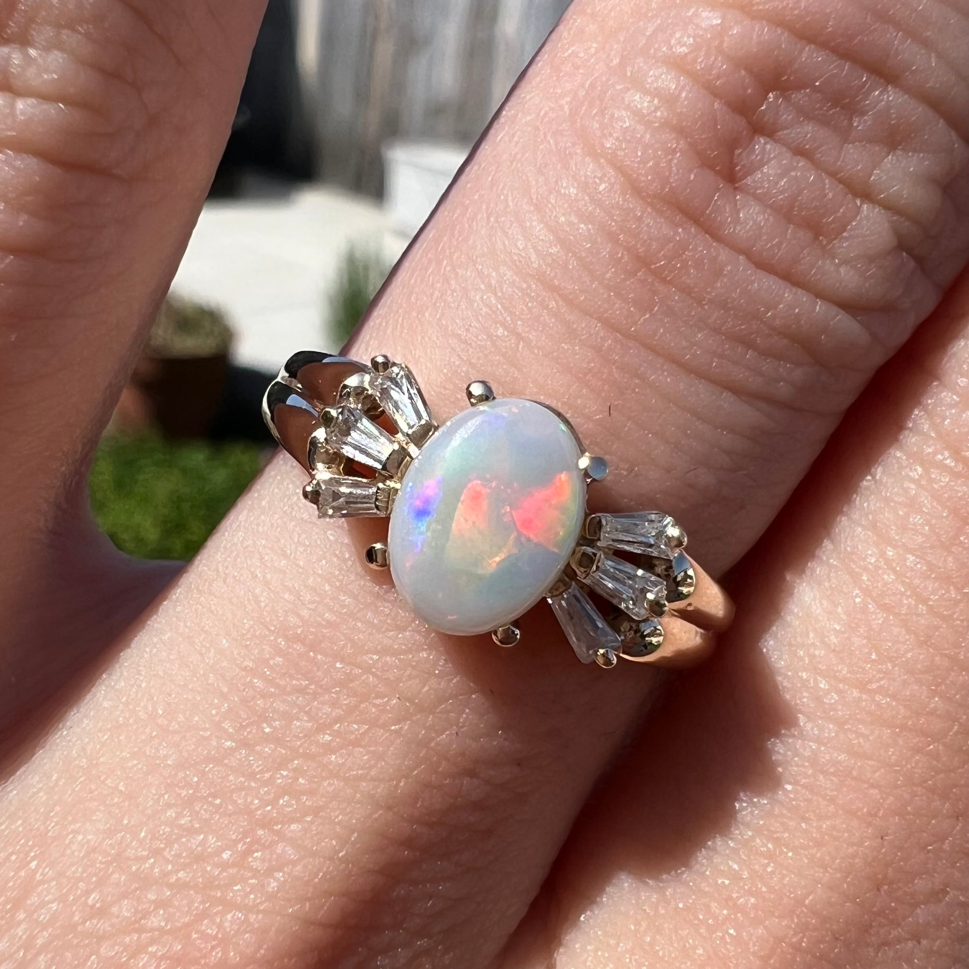 A yellow gold ring set with a natural Australian opal and tapered baguette cut cubic zirconia accents.