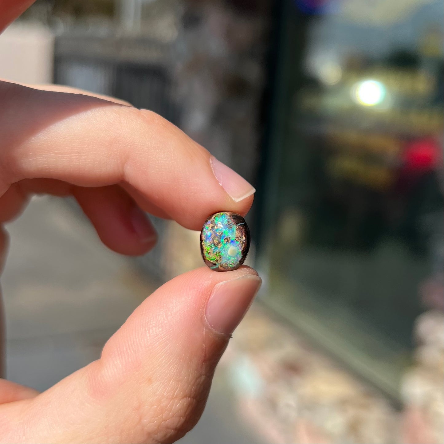 An oval cabochon cut boulder opal stone with green and blue color play.