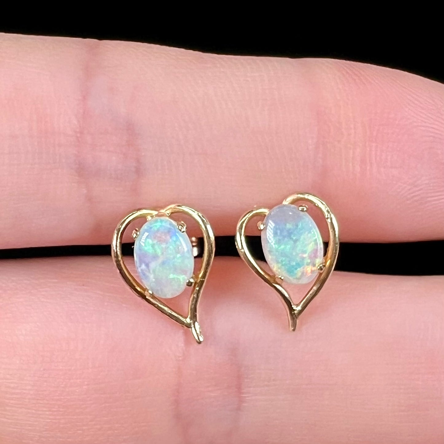 A pair of yellow gold, heart shaped stud earrings set with oval cabochon cut natural opal stones.