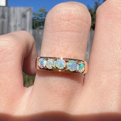 An 18 karat yellow gold line-style filigree ring mounted with five round, cabochon cut Australian crystal opals.